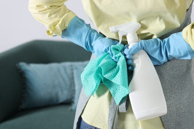 Photo of Woman hiding spray bottle of cleaning product and rag behind her back indoors, closeup. Space for text