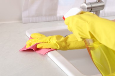 Photo of Woman using cleaning product while wiping sink with rag in kitchen, closeup