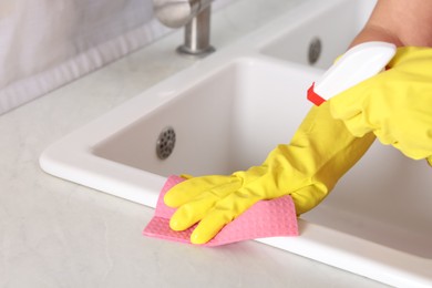 Photo of Woman using cleaning product while wiping sink with rag in kitchen, closeup