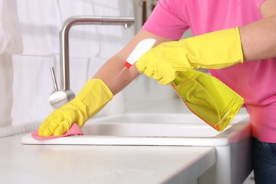 Photo of Woman using cleaning product while wiping sink with rag in kitchen, closeup