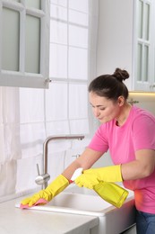 Photo of Woman using cleaning product while wiping sink with rag in kitchen