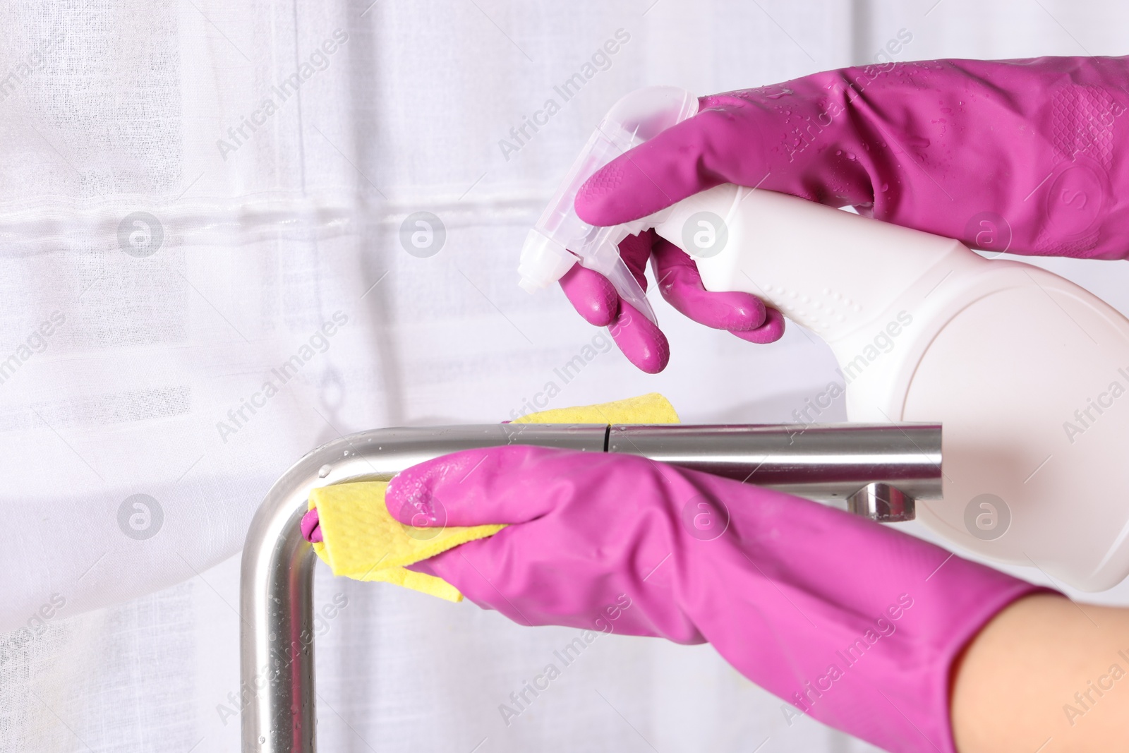 Photo of Woman using cleaning product while wiping faucet of kitchen sink with rag indoors, closeup