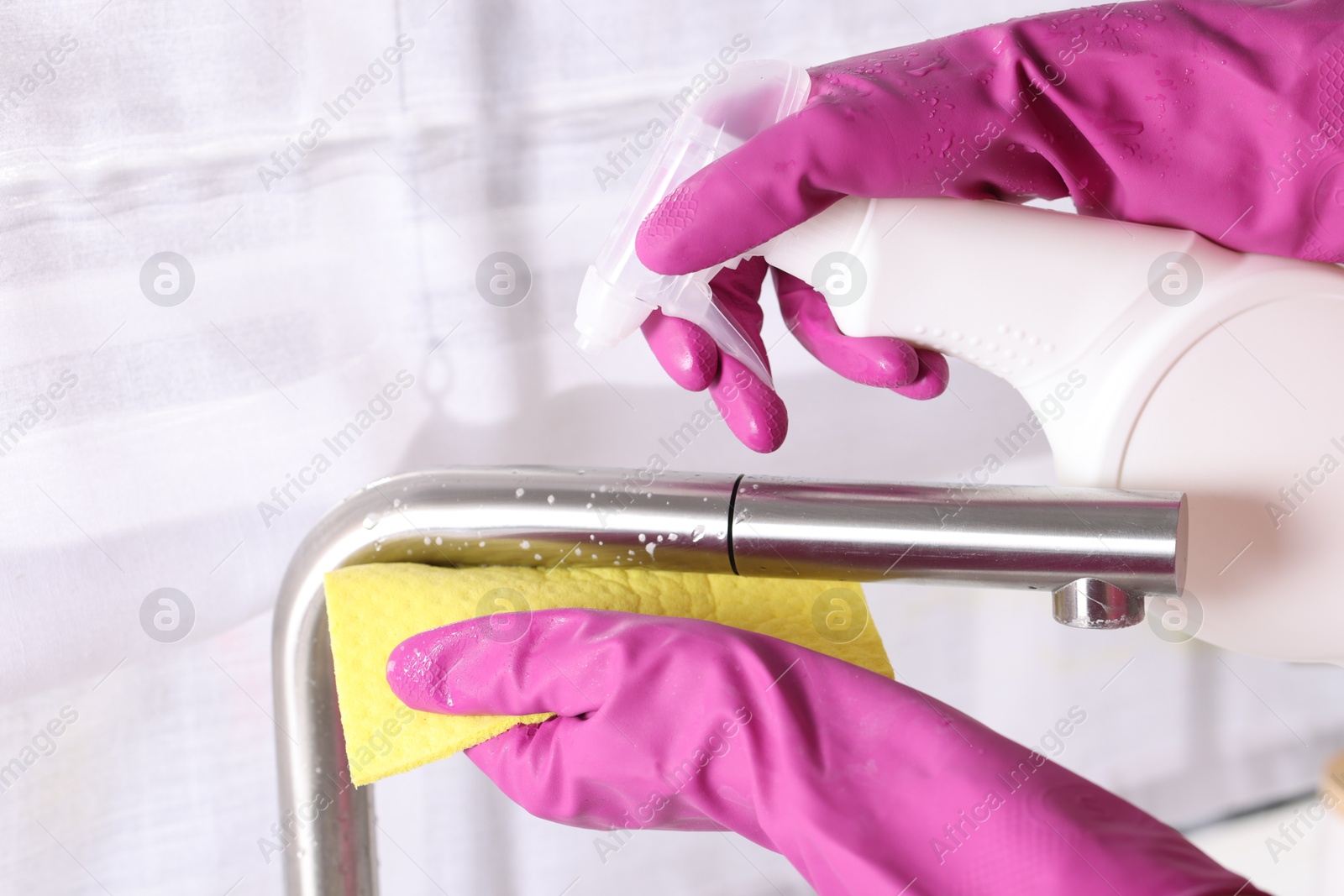 Photo of Woman using cleaning product while wiping faucet of kitchen sink with rag indoors, closeup