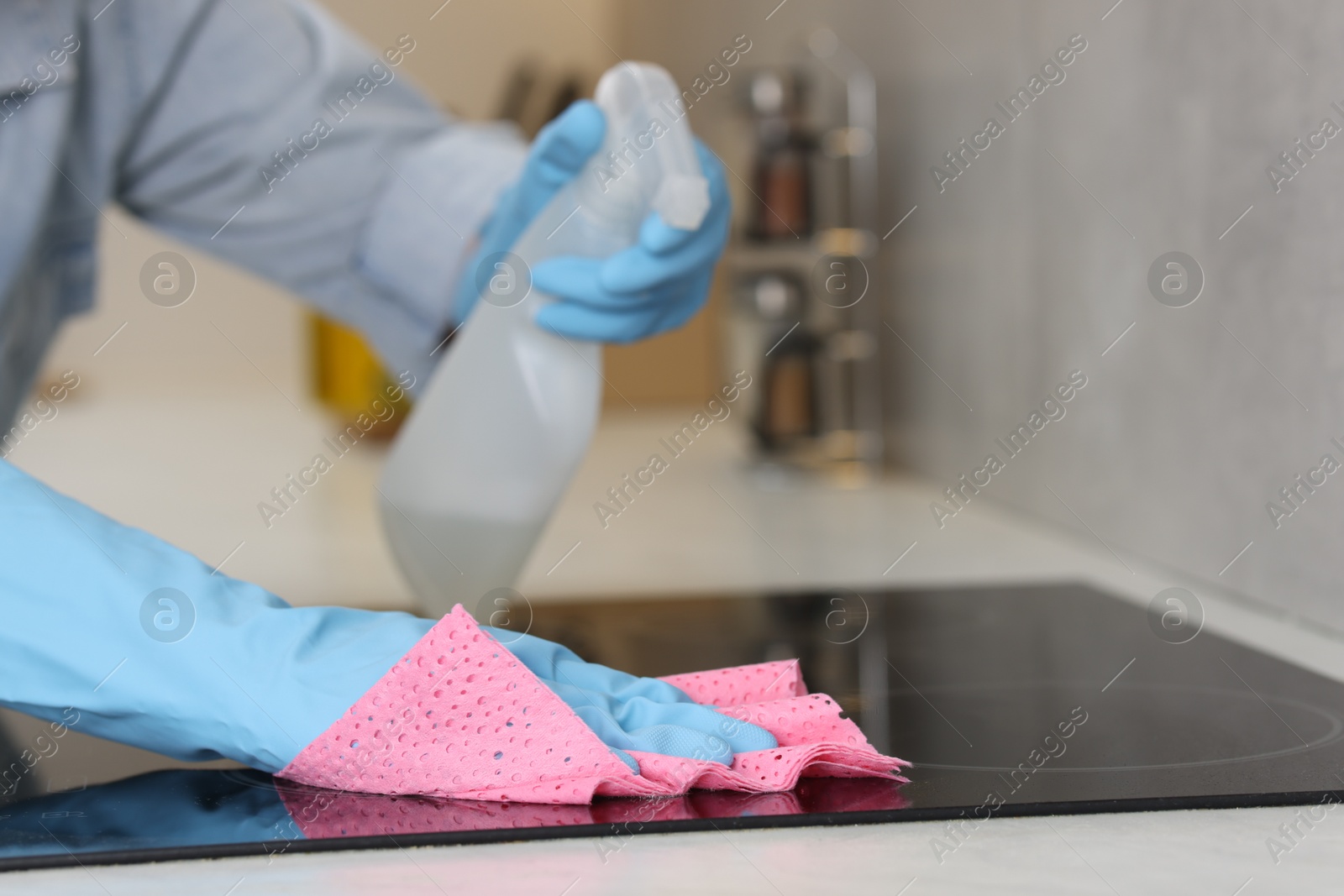 Photo of Woman using cleaning product while wiping induction cooktop with rag in kitchen, closeup. Space for text