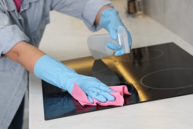 Photo of Woman using cleaning product while wiping induction cooktop with rag in kitchen, closeup