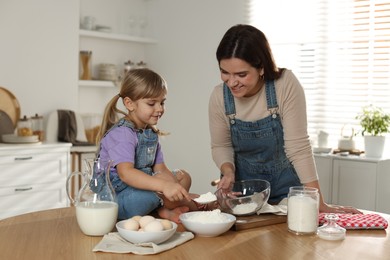 Photo of Little girl helping her mom making dough at table in kitchen