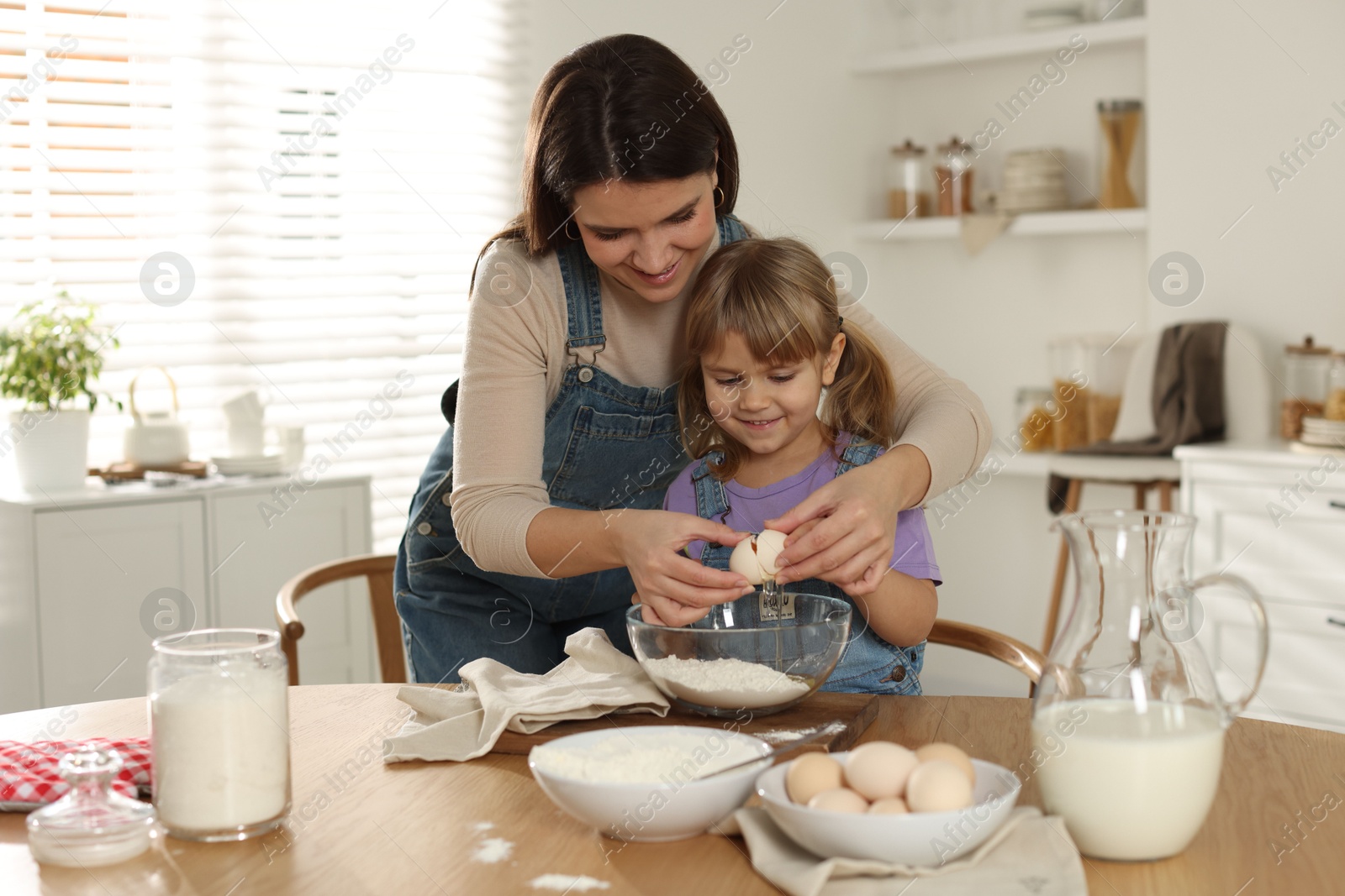 Photo of Little girl helping her mom making dough at table in kitchen