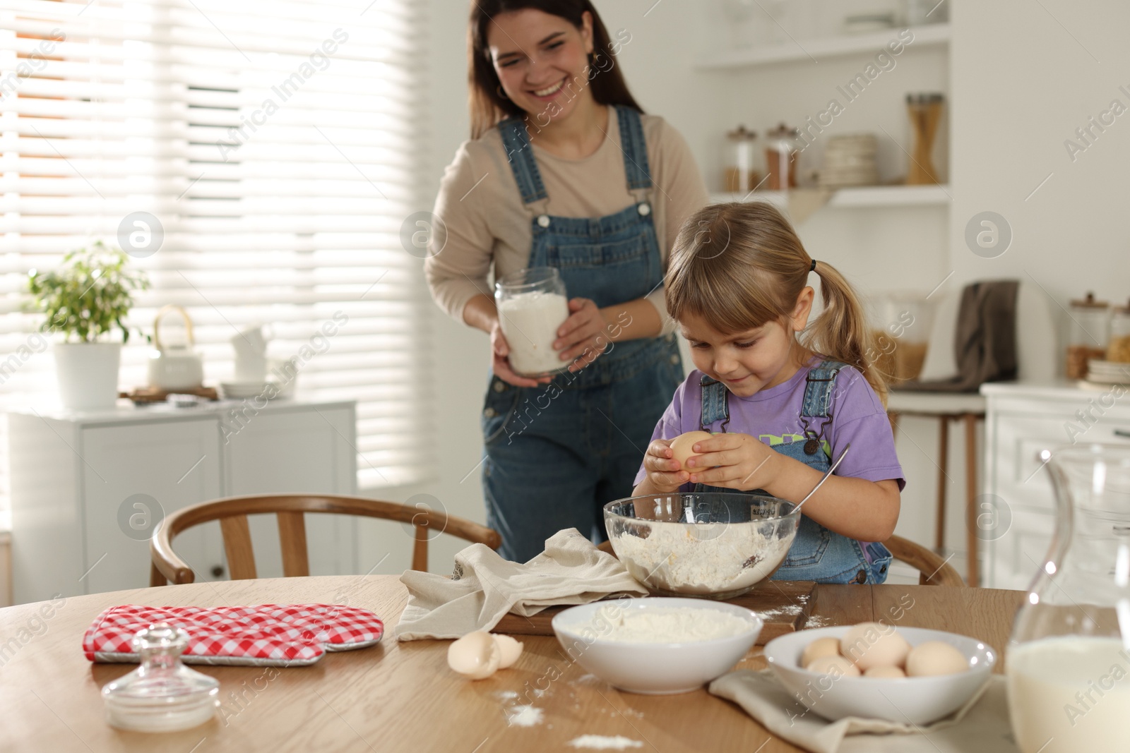 Photo of Little girl helping her mom making dough at table in kitchen