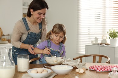 Photo of Little girl helping her mom making dough at table in kitchen, space for text