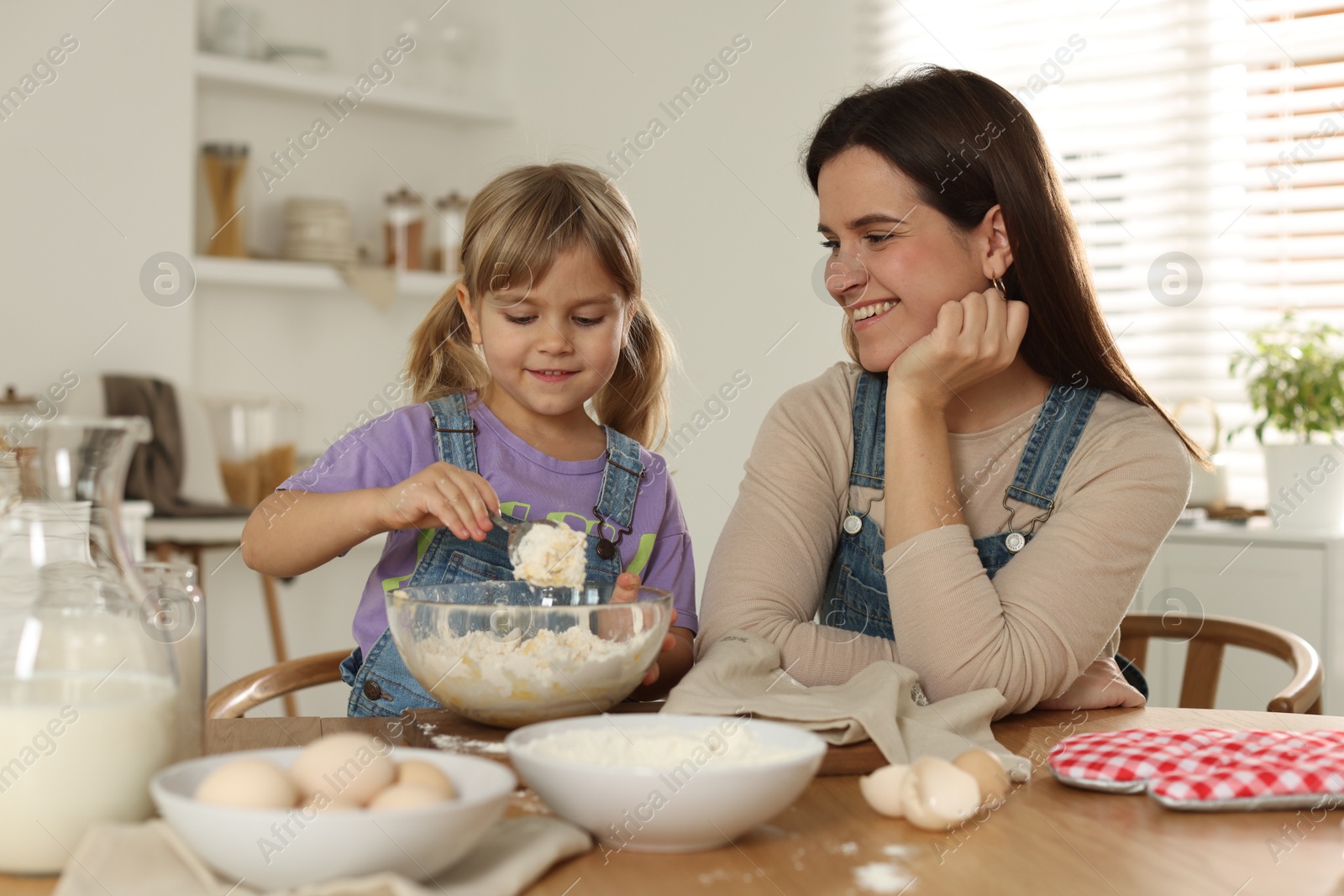 Photo of Little girl helping her mom making dough at table in kitchen