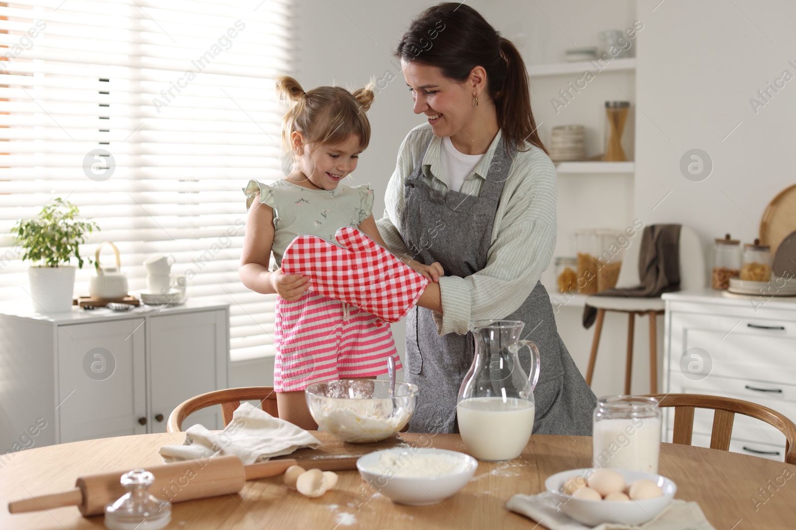 Photo of Mother with her little daughter cooking together at table in kitchen