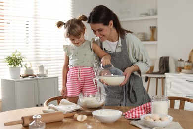 Photo of Little girl helping her mom making dough at table in kitchen