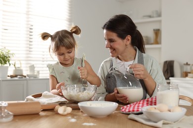 Photo of Little girl helping her mom making dough at table in kitchen