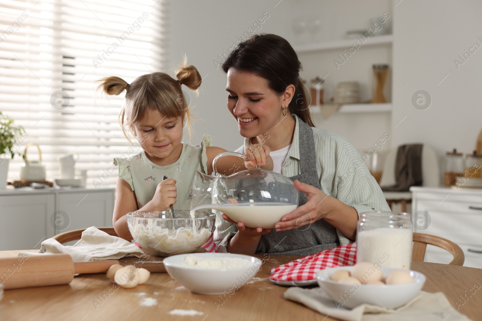 Photo of Little girl helping her mom making dough at table in kitchen