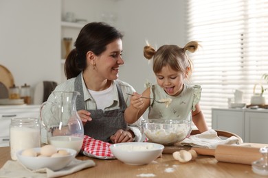 Photo of Little girl helping her mom making dough at table in kitchen