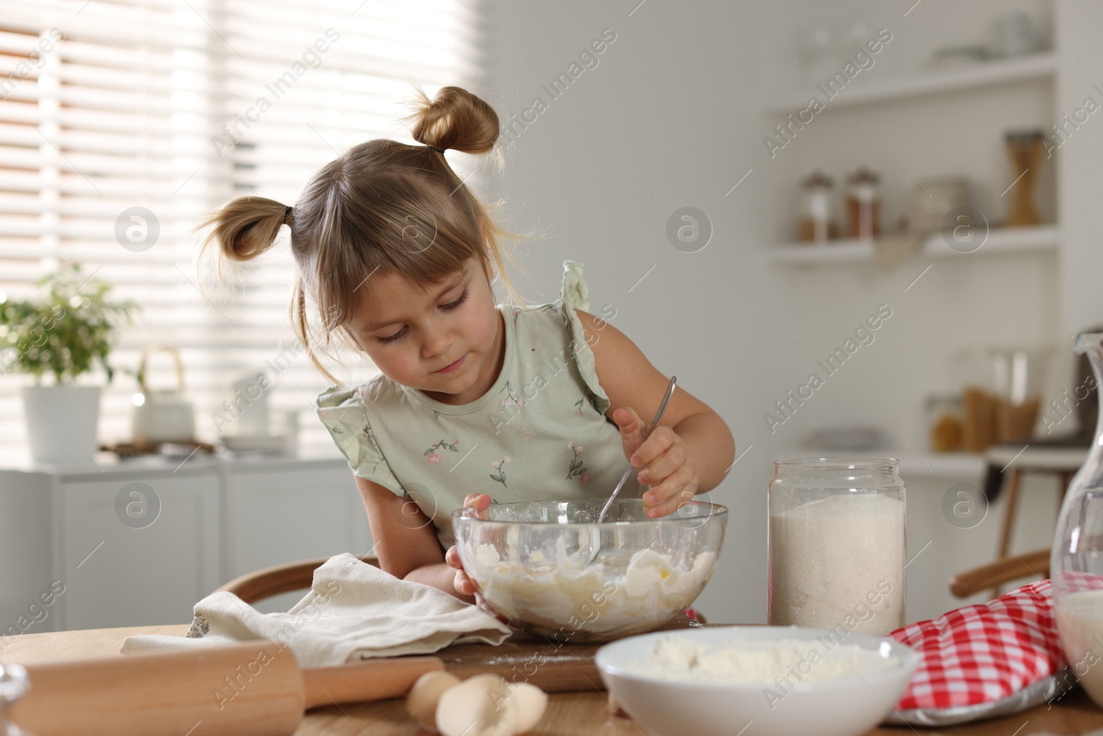 Photo of Little helper. Cute girl making dough at table in kitchen