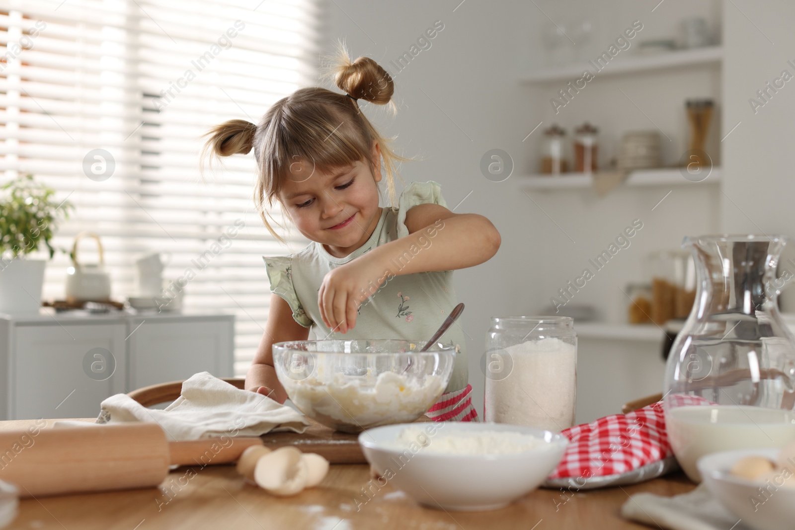 Photo of Little helper. Cute girl making dough at table in kitchen