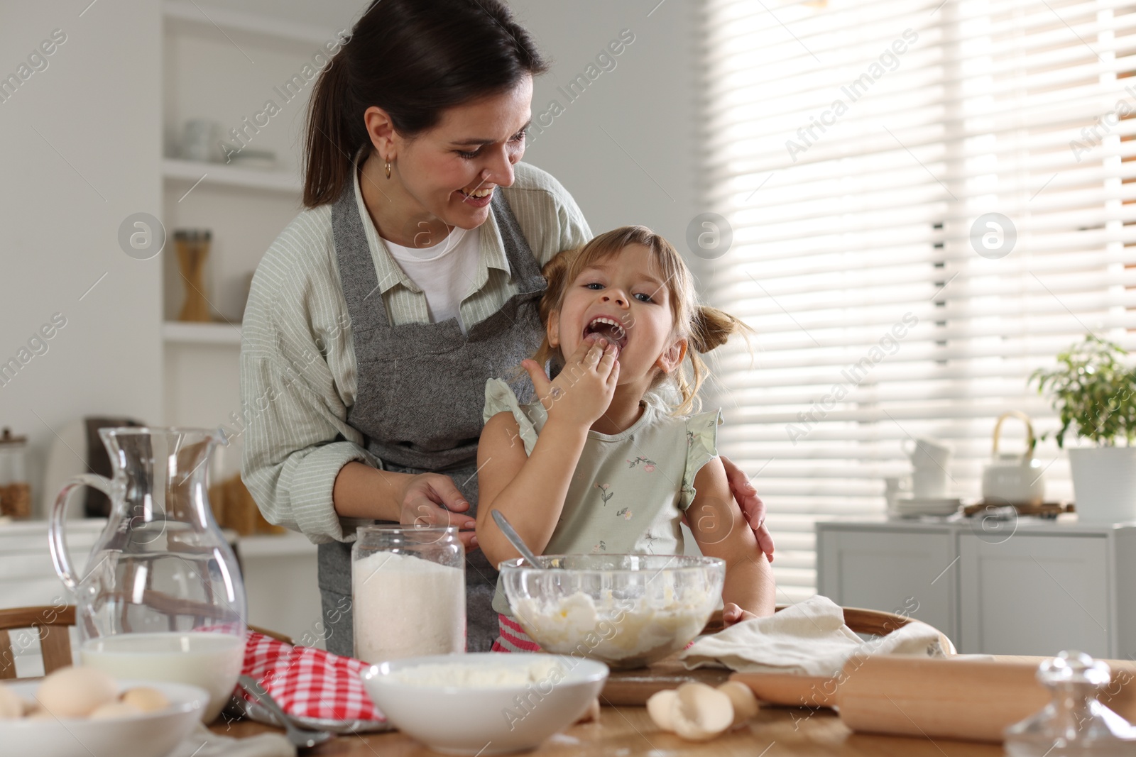 Photo of Little girl helping her mom making dough at table in kitchen