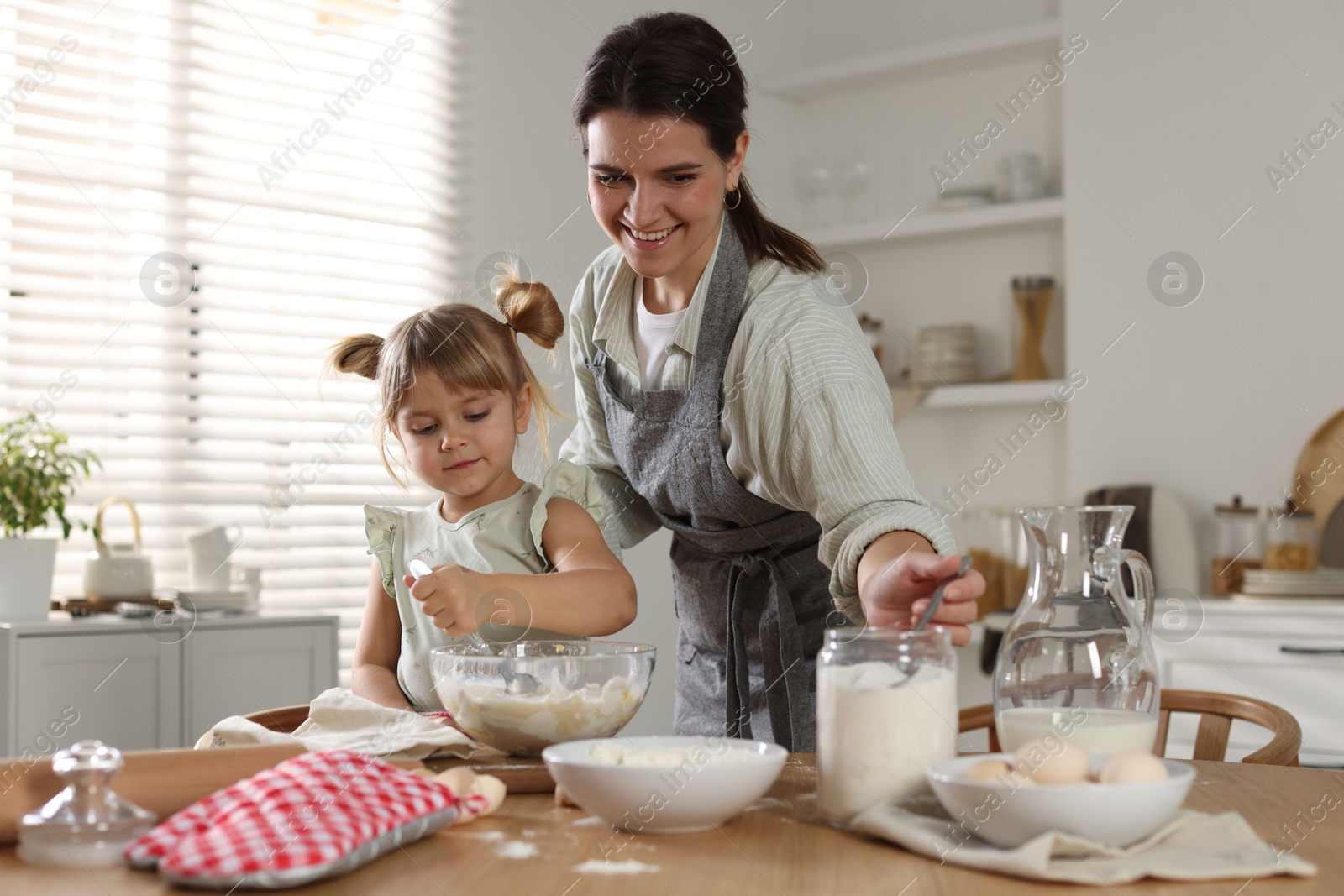 Photo of Little girl helping her mom making dough at table in kitchen