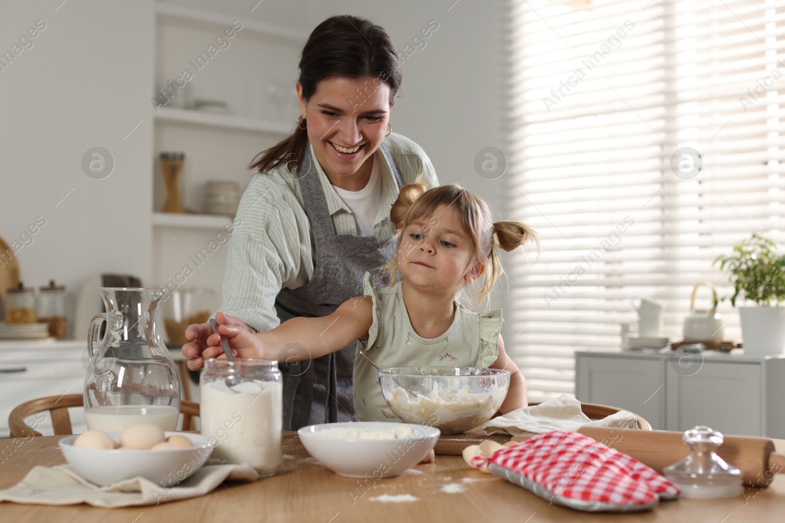 Photo of Little girl helping her mom making dough at table in kitchen