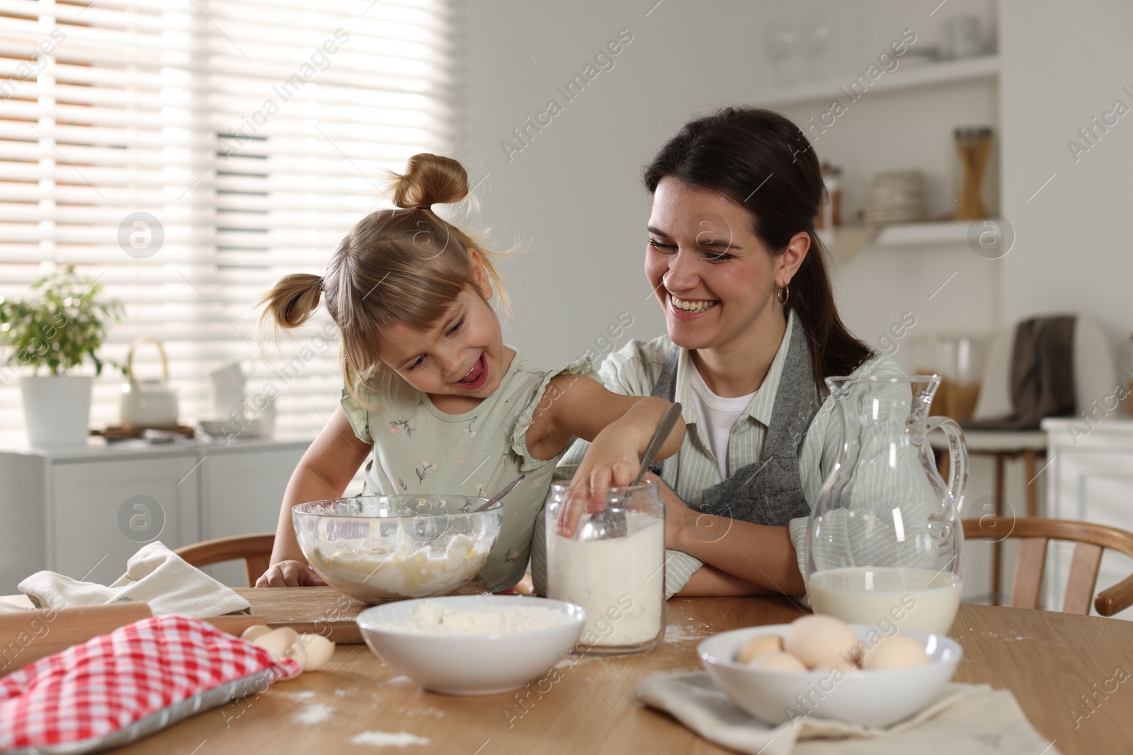 Photo of Little girl helping her mom making dough at table in kitchen