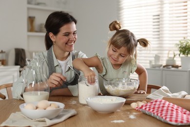 Photo of Little girl helping her mom making dough at table in kitchen