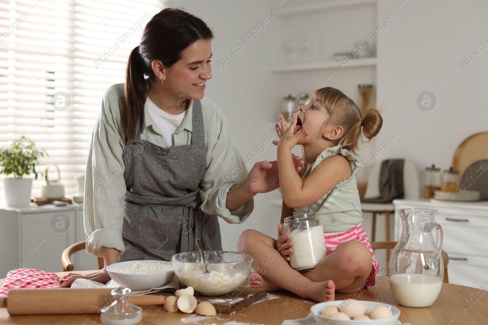 Photo of Little girl helping her mom making dough at table in kitchen