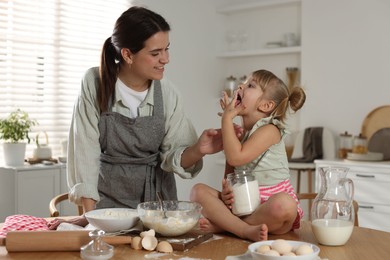 Little girl helping her mom making dough at table in kitchen