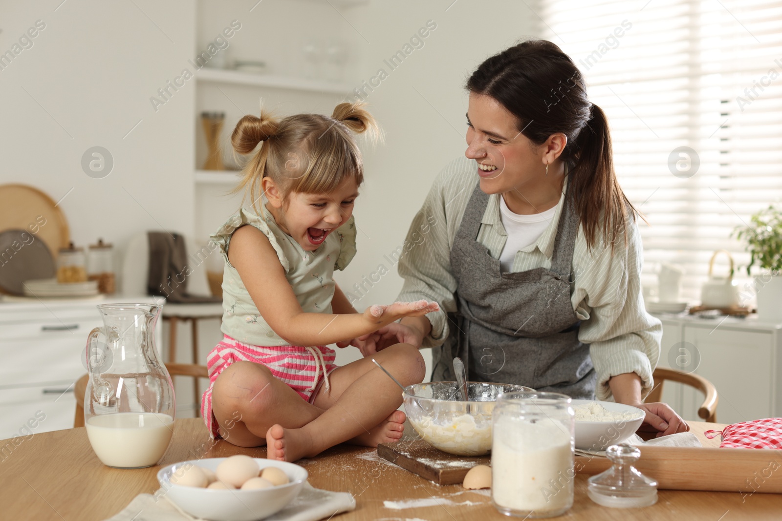 Photo of Little girl helping her mom making dough at table in kitchen