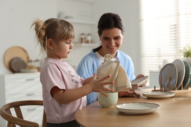 Photo of Little girl helping her mom wiping plates at table in kitchen