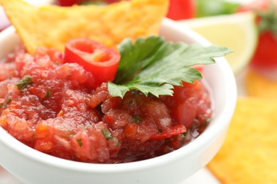 Spicy salsa in bowl and nachos on table, closeup