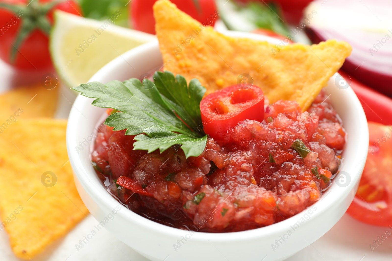 Photo of Spicy salsa in bowl, nachos and ingredients on table, closeup