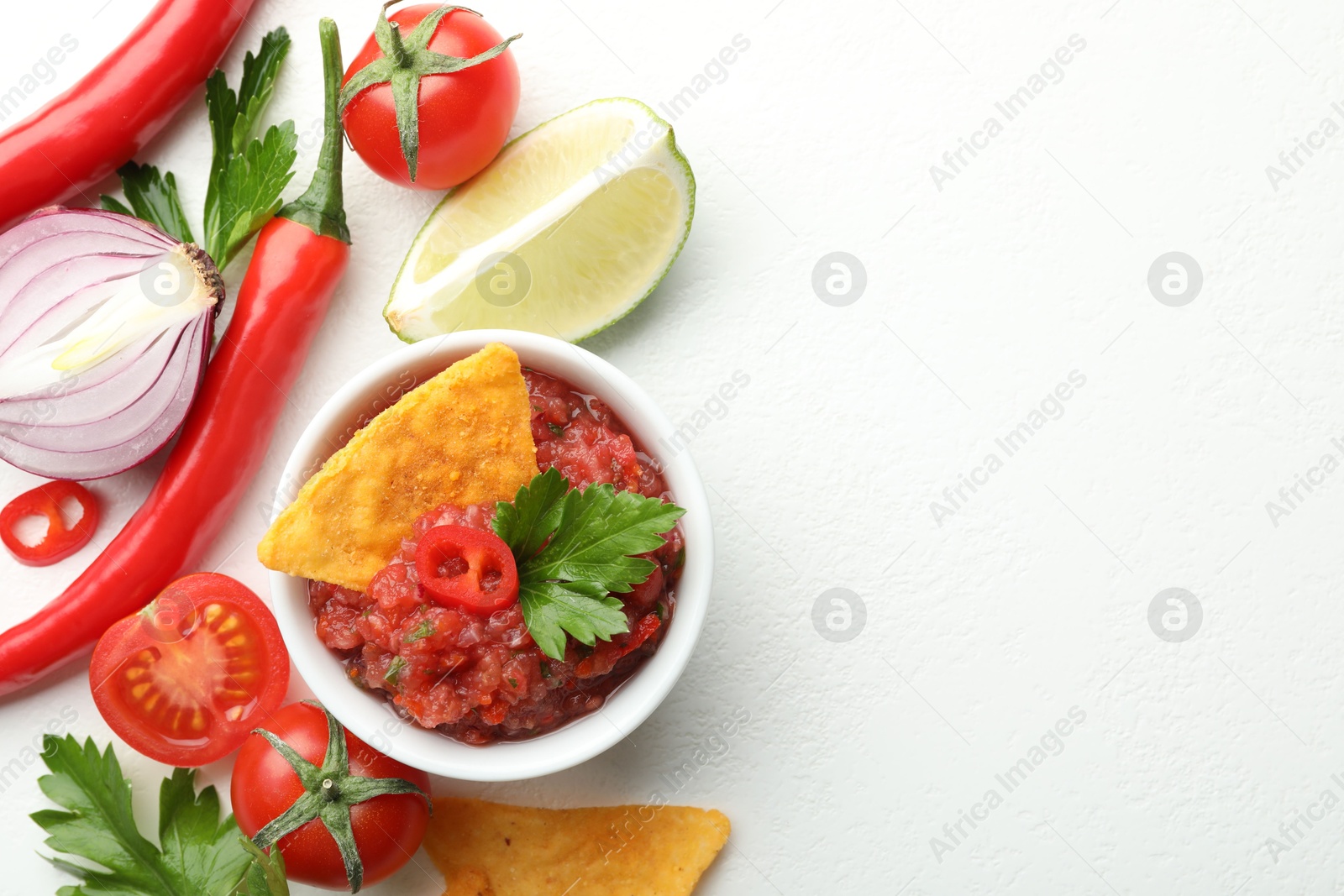 Photo of Spicy salsa in bowl, nachos and ingredients on white table, flat lay. Space for text