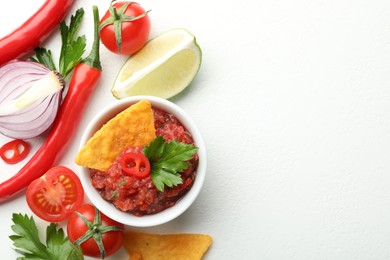 Spicy salsa in bowl, nachos and ingredients on white table, flat lay. Space for text