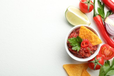 Photo of Spicy salsa in bowl, nachos and ingredients on white table, flat lay. Space for text