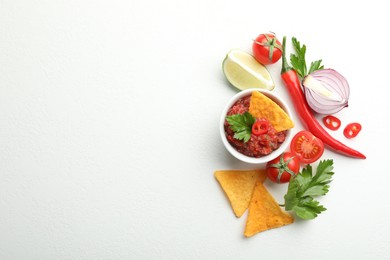 Photo of Spicy salsa in bowl, nachos and ingredients on white table, flat lay. Space for text