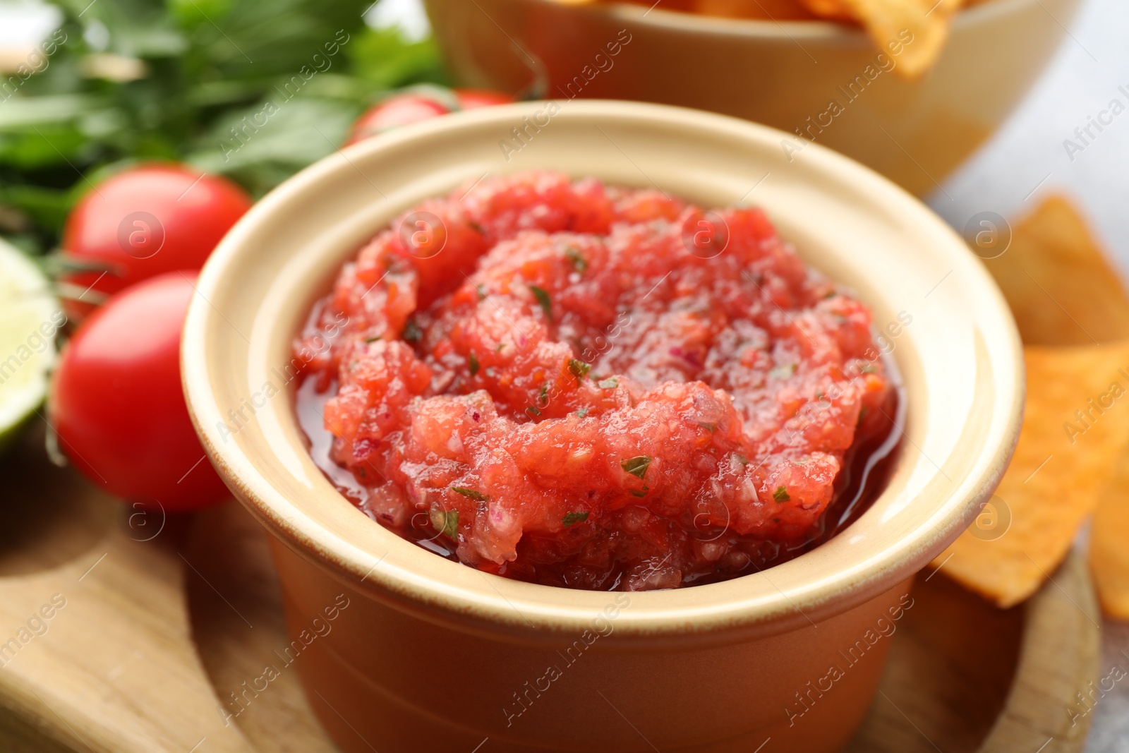 Photo of Spicy salsa in bowl, nachos and ingredients on table, closeup