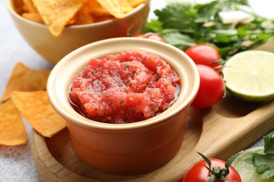 Spicy salsa in bowl, nachos and ingredients on table, closeup