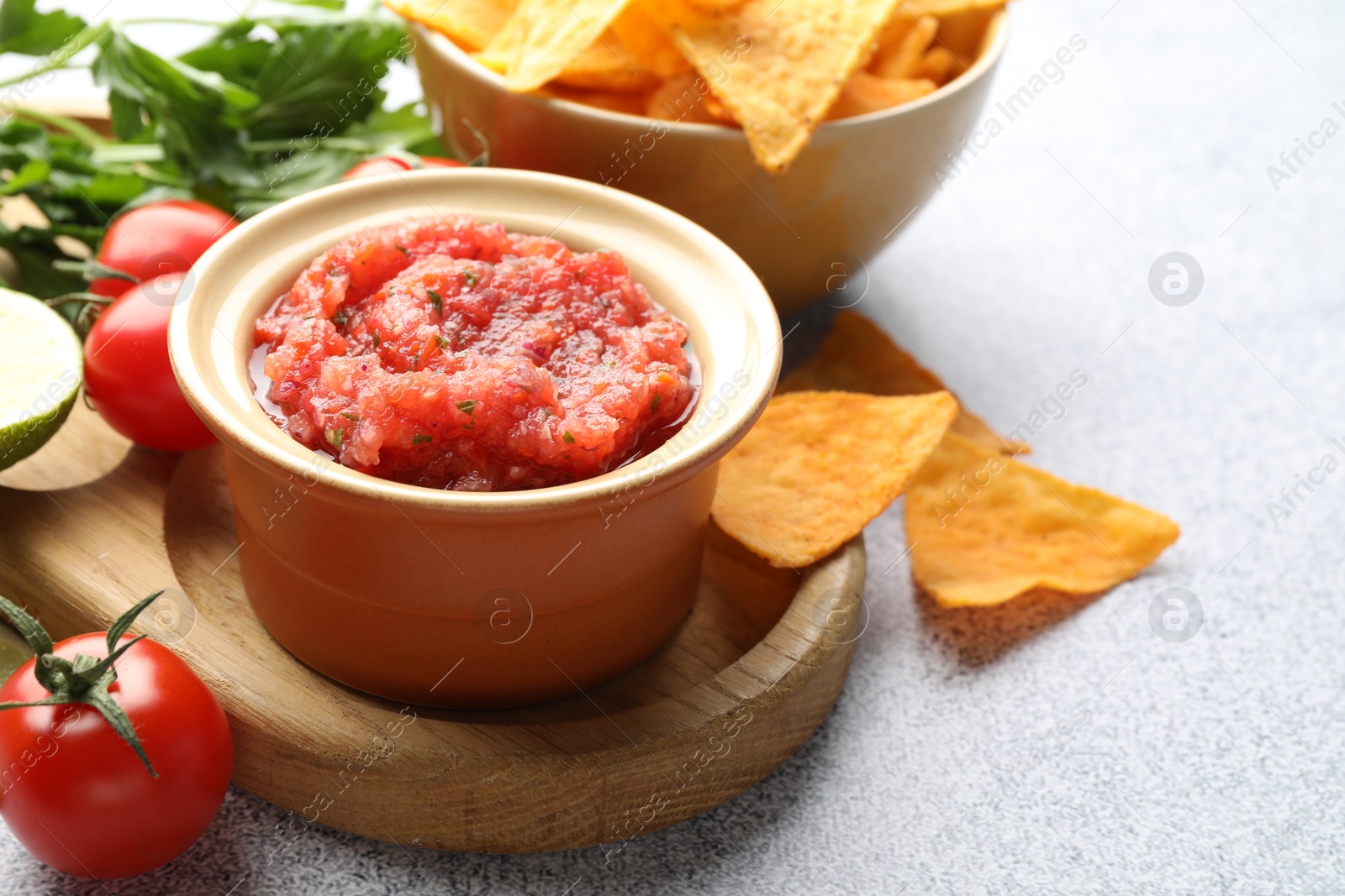 Photo of Spicy salsa in bowl, nachos and ingredients on light grey table, closeup. Space for text