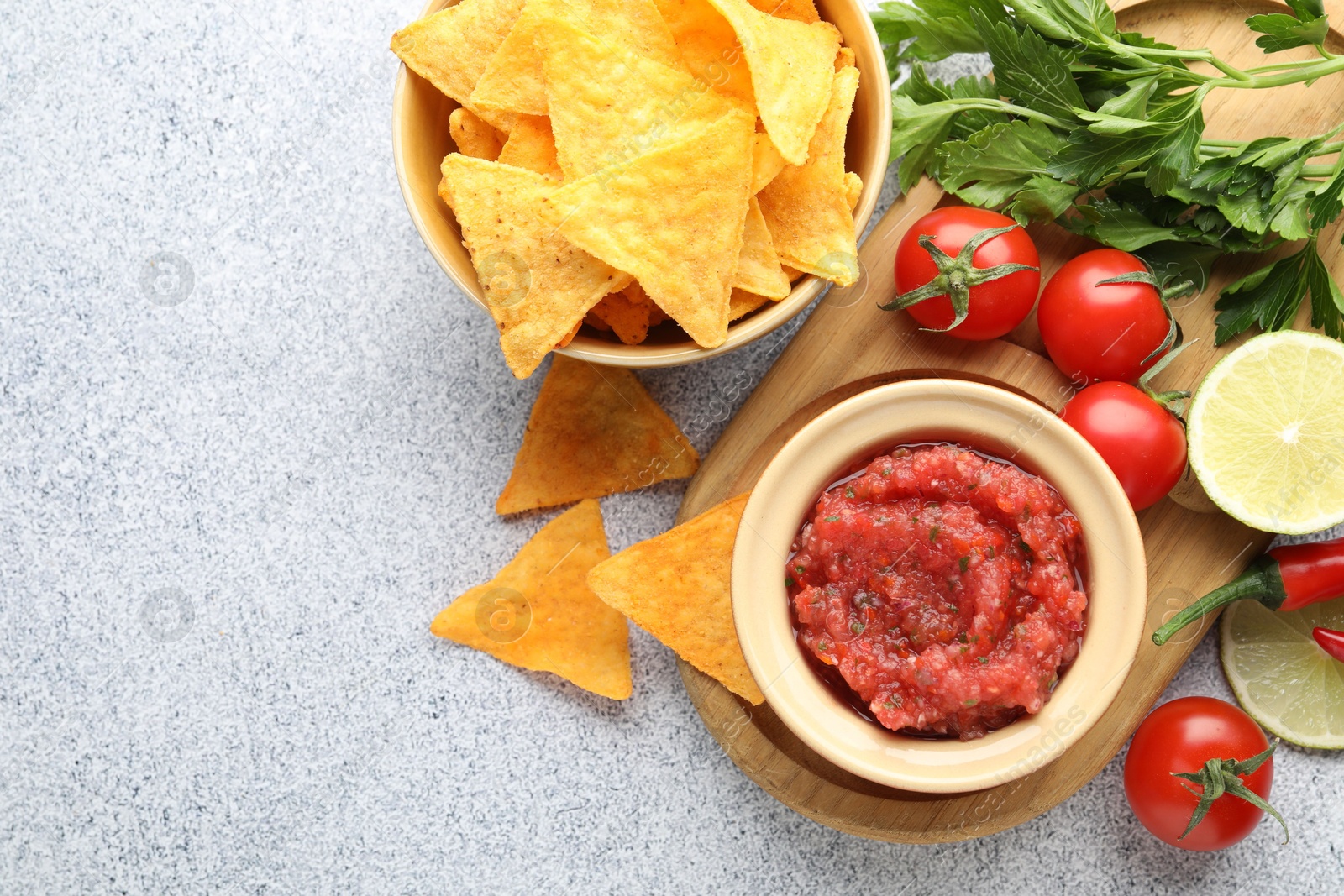 Photo of Spicy salsa in bowl, nachos and ingredients on light grey table, flat lay. Space for text