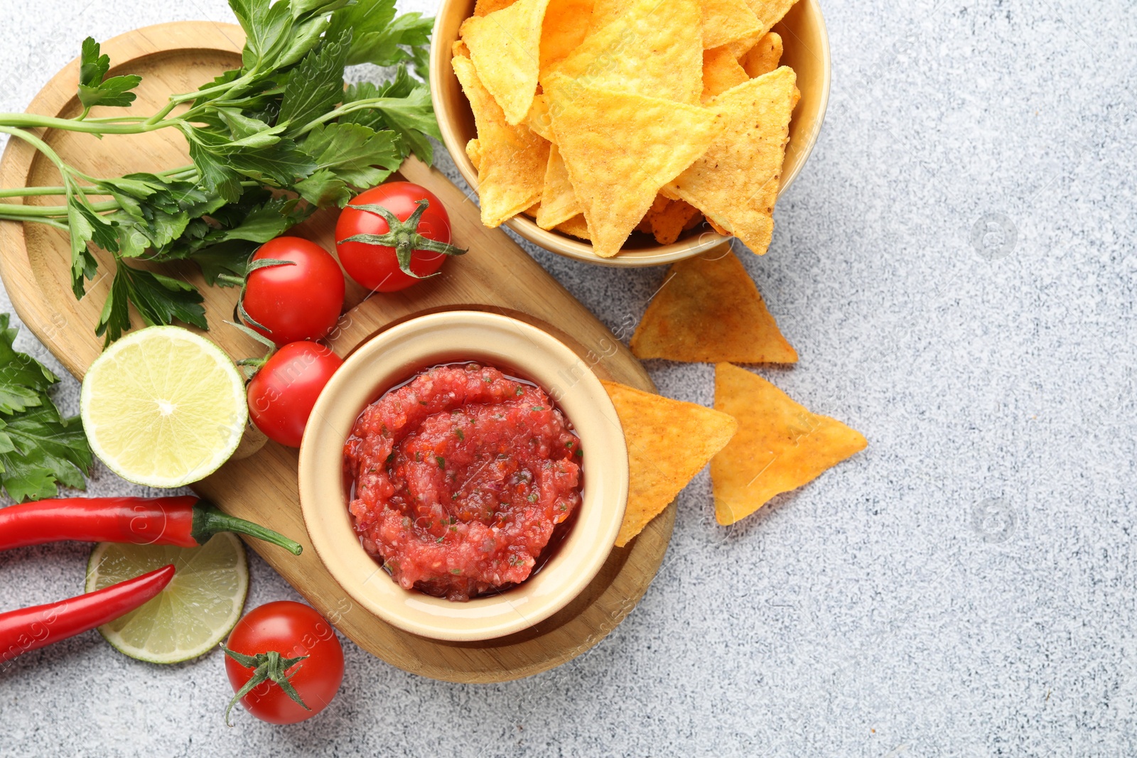 Photo of Spicy salsa in bowl, nachos and ingredients on light grey table, flat lay. Space for text