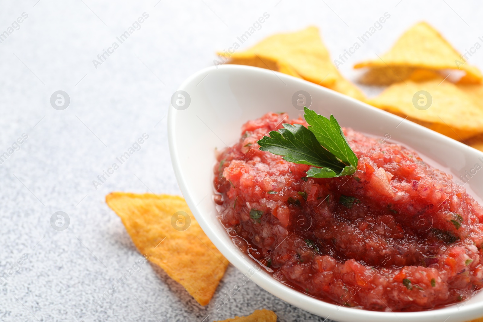 Photo of Spicy salsa in gravy boat and nachos on light grey table, closeup. Space for text