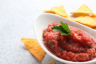 Spicy salsa in gravy boat and nachos on light grey table, closeup. Space for text