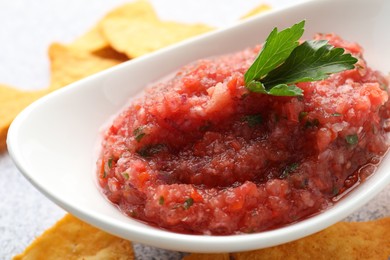 Photo of Spicy salsa in gravy boat and nachos on table, closeup