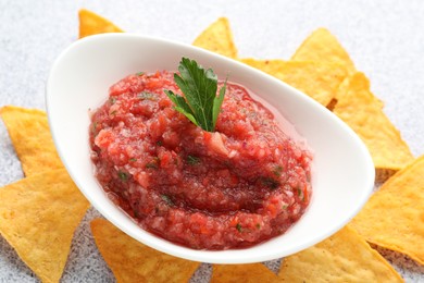 Spicy salsa in gravy boat and nachos on light grey table, closeup