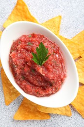 Spicy salsa in gravy boat and nachos on light grey table, flat lay