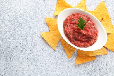 Photo of Spicy salsa in gravy boat and nachos on light grey table, flat lay. Space for text