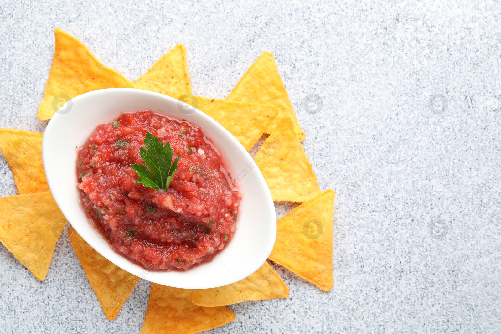 Photo of Spicy salsa in gravy boat and nachos on light grey table, flat lay. Space for text