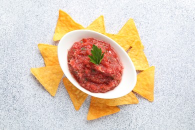 Spicy salsa in gravy boat and nachos on light grey table, flat lay