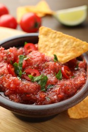 Photo of Spicy salsa in bowl and nacho chip on table, closeup